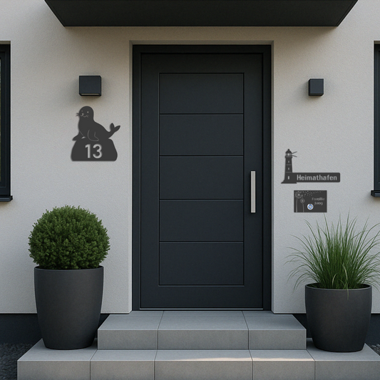 Moodbild: Seehund-Hausnummer, maritimes Schild „Heimathafen“ und personalisierte Türklingel – alle aus V2A Edelstahl, anthrazit pulverbeschichtet – modern montiert an Eingangstür
