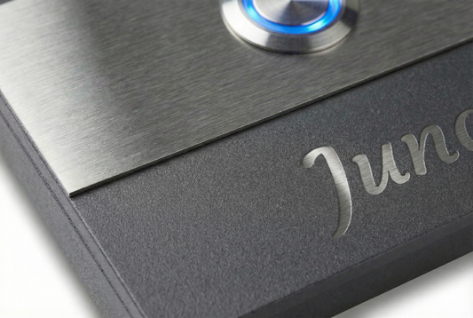 Detailaufnahme der Aufputztürklingel „Bremen“ in Anthrazit mit gebürsteter Edelstahlplatte, blauer LED am Klingeltaster und Gravur.