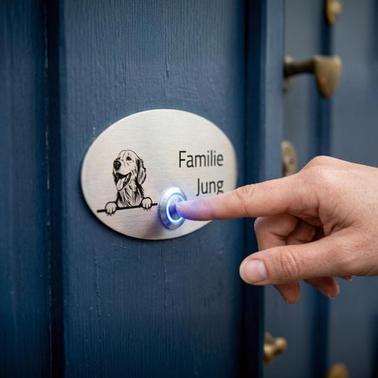 Hand drückt ovale Edelstahl-Türklingel Rom mit Hundemotiv und Gravur „Familie Jung“ an blauer Haustür.