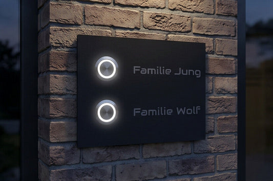 Anthrazitfarbene Frankfurt Zweifamilienhaus-Türklingel mit beleuchteten LED-Tastern an einer Ziegelwand bei Abendlicht