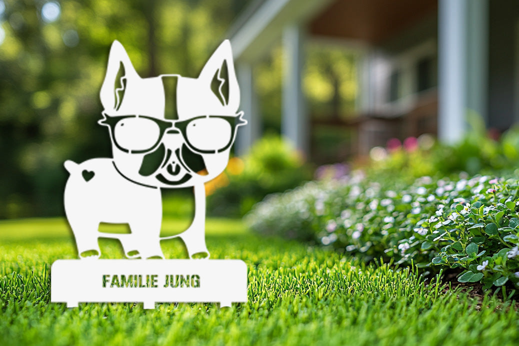 Weiß pulverbeschichteter Gartenstecker aus Edelstahl in Form einer Bulldogge mit Sonnenbrille und dem Schriftzug „Familie Jung“ – stilvoll im grünen Vorgarten platziert.
