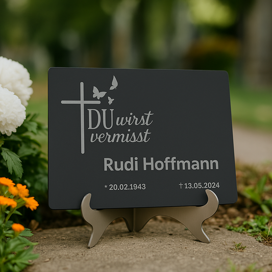 Gedenktafel in Anthrazit mit Gravur „DU wirst vermisst“, montiert auf einem Edelstahl-Schilderständer im Freien – mit Name Rudi Hoffmann und Datum
