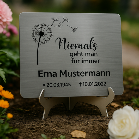 Gedenktafel aus Edelstahl mit Gravur „Niemals geht man für immer“, montiert auf Schilderständer – Name Erna Mustermann, Geburts- und Sterbedatum im Blumenumfeld
