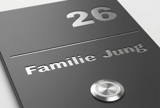 Detailaufnahme einer anthrazitfarbenen Edelstahl-Türklingel mit Hausnummer „26“, Namensgravur „Familie Jung“ und rundem Klingeltaster.