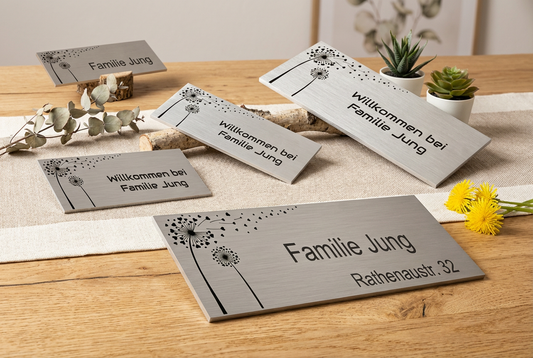 Edelstahlschild mit Pusteblumen-Motiv und Wunschtext auf Holztisch mit Deko arrangiert.